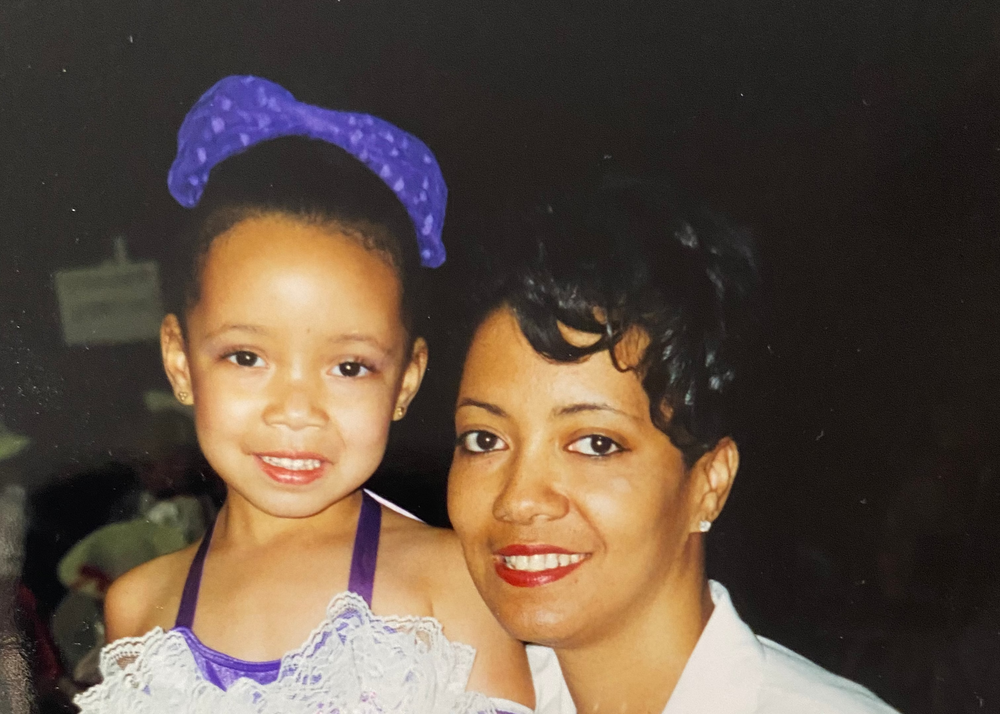 Woman and young girl in a purple dress with a blue bow posing together.
